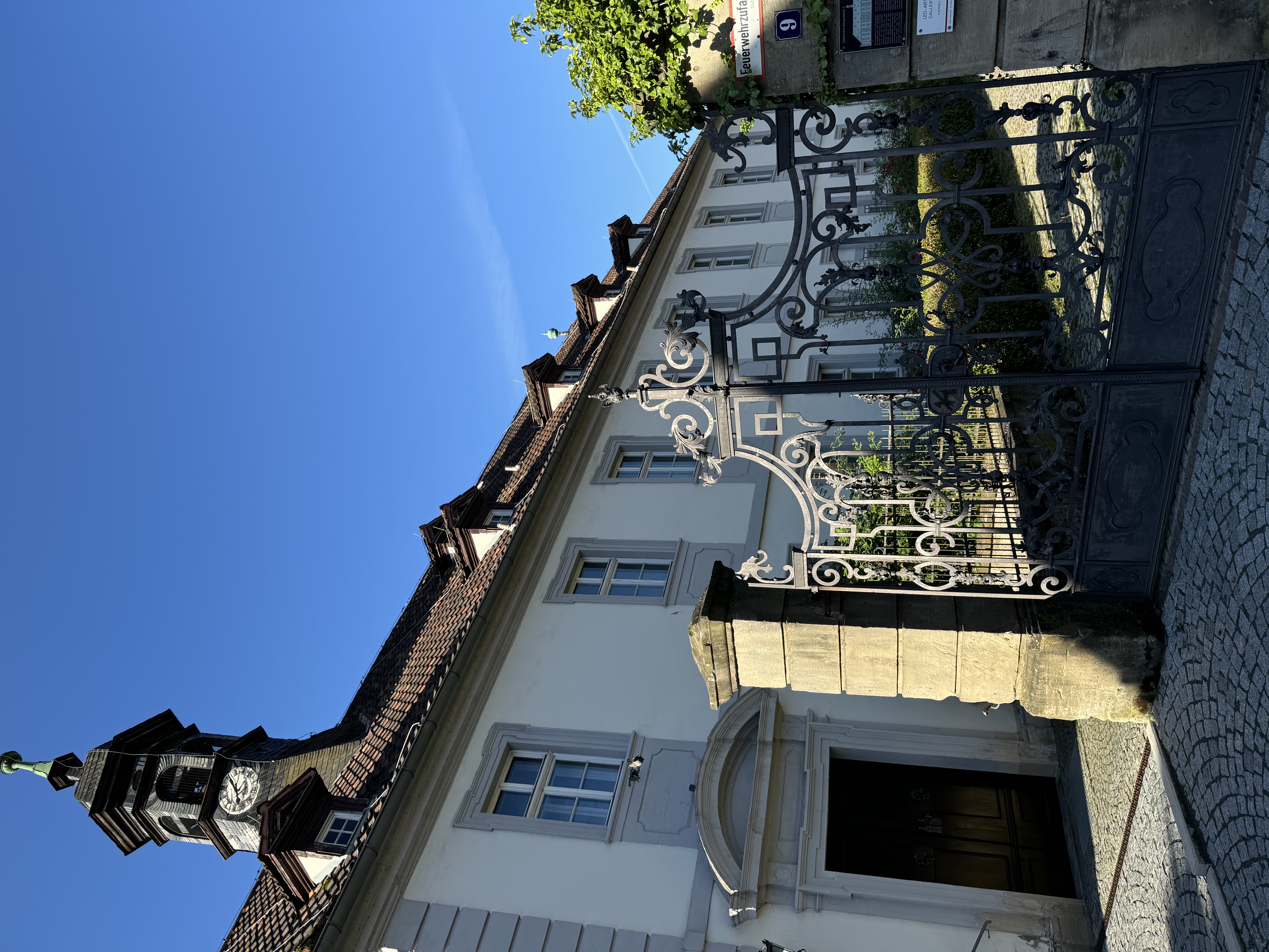 zu sehen ist ein älteres Gebäude mit einer Turmuhr und einem schmiedeeisernen Tor