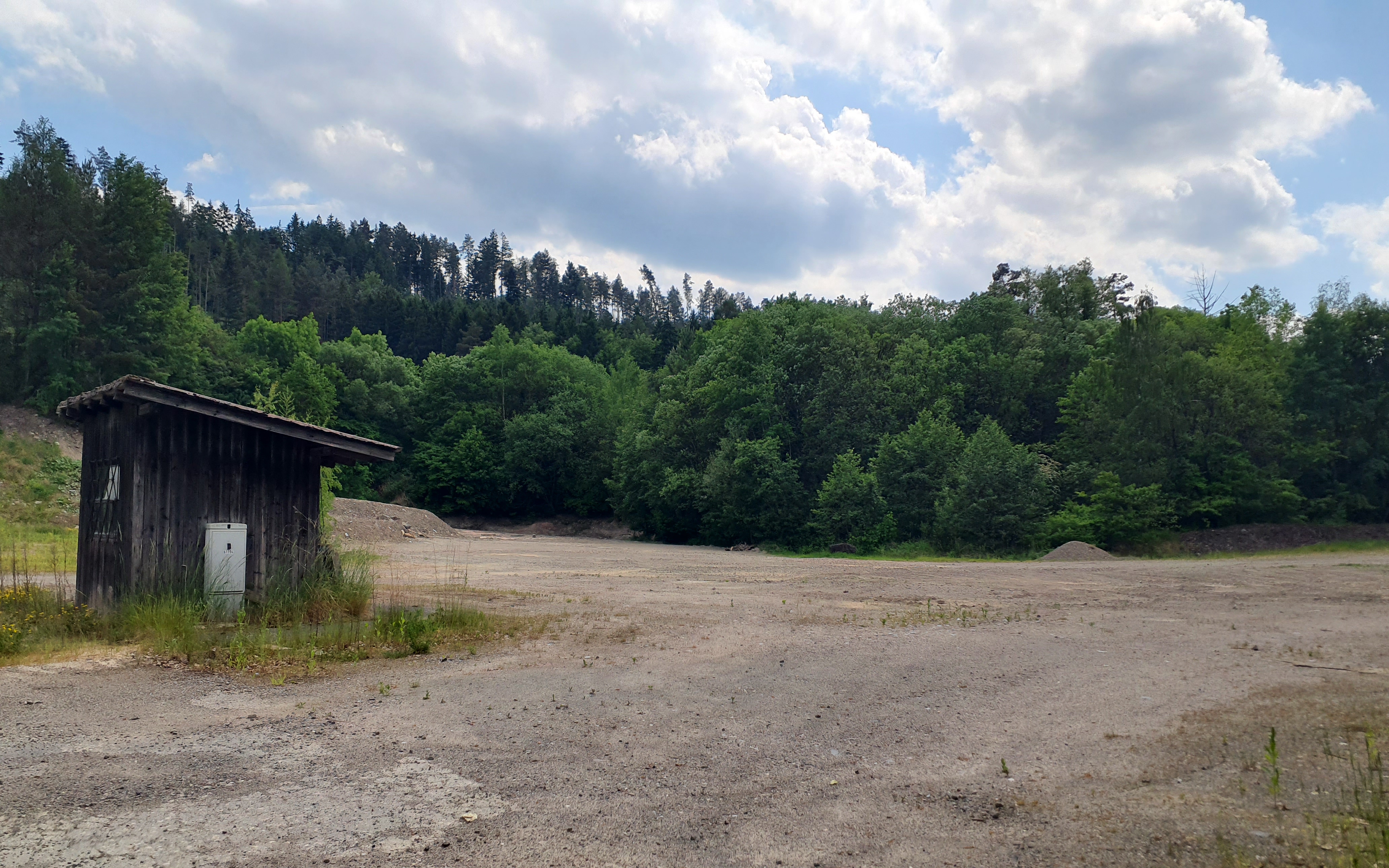 eine brache Fläche, dahinter Wald und ein einsames Häuschen sind zu sehen